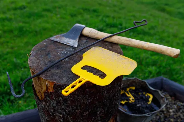 Ahşap bir kütük, bir balta, bir kanca ve parlak sarı ızgara alet dahil olmak üzere çeşitli yemek ve açık hava araçları, hepsi yemyeşil bir çim arazi karşı kurulur.
