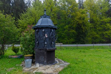 Bu görüntüde süslü metal işçiliğiyle süslenmiş büyüleyici bir vintage su sergileniyor, yeşil ve dingin doğanın canlı bir zeminine karşı kurulmuş, davetkar yansıma ve huzur.
