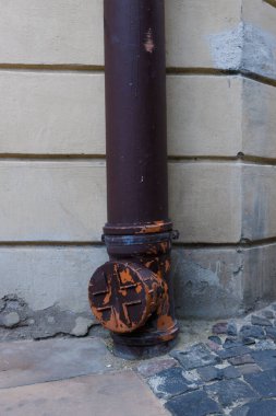 Bu resim, eskimiş boyasıyla etkileyici bir kırsal dokunuşu ve zeminle buluştuğu yerde karmaşık bir tasarımı gösteren kahverengi bir drenaj borusunu içeriyor..