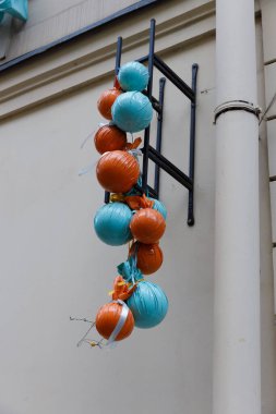 This image features a striking arrangement of blue and orange decorative balls suspended on a black metal framework against a light-colored wall. A cheerful urban detail.