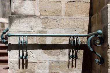 This photograph showcases a beautifully designed iron handrail affixed to a textured stone wall, highlighting its artistic curves and functional design in a captivating urban environment.