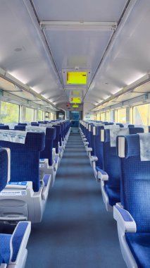 Bu görüntü modern bir trenin yolcu kabininin içini gösteriyor, rahat mavi koltuklar ve geniş yan pencerelerden bol miktarda doğal ışık..