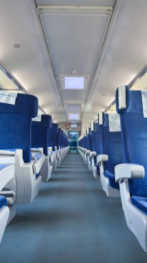 Görüntü, düzgün düzenlenmiş mavi koltukları, geniş koridoru ve yüksek teknolojili ışıklandırması olan bir tren vagonunun içini gösteriyor. Gezginler için davetkar bir atmosfer yaratıyor..