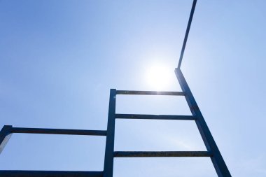 Görüntü, parlak bir güneşe doğru bakan bir merdiven sergiliyor, dingin mavi gökyüzüne doğru batıyor, kişinin hayattaki hedeflerine ve amaçlarına ulaşma yolculuğunu temsil ediyor..