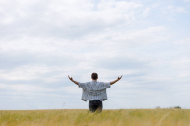Bu huzurlu görüntüde, bir adam geniş bir alanda duruyor, kolları ardına kadar açık, gökyüzünün ve doğanın güzelliği içinde, özgürlükle ve dışarıyla olan bağlantıyı simgeliyor..