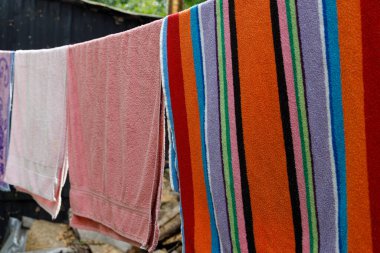 Açık havada asılı renkli havlulardan oluşan bir sıra, çeşitli desenler ve canlı renkler sergiliyor. Havlular, konfor ve yaz atmosferini vurgulayan dokuların bir kombinasyonunu sergiliyor..