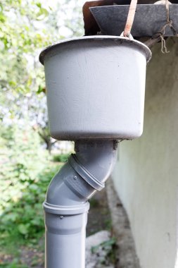 Bu resim, yağmur suyunu binadan uzaklaştırmak için tasarlanmış, etkili drenajın temel elementlerini vurgulayan, bir binaya bağlı gri bir oluk sistemi gösteriyor..