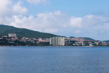 Parlak sularla kaplanmış çarpıcı bir sahil manzarası. Gök mavisi yansıyor, bereketli dağlarla çerçevelenmiş, modern mimarinin doğal güzellikler arasında bir karışımını gösteriyor..