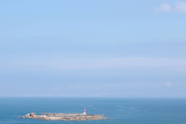 Bu resim, engin okyanus sularının ortasında berrak mavi bir gökyüzünün altında canlı bir deniz fenerinin bulunduğu sakin bir sahneyi gösteriyor..