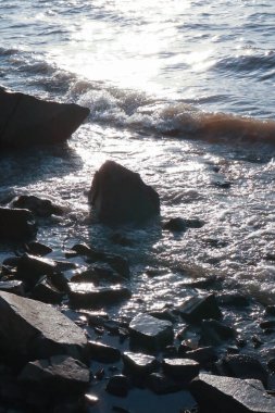 Yumuşak dalgaların kayaların üzerinde yükseldiği, güneş ışığını güzel yansıtan, huzurlu bir kıyı şeridi manzarası. Suyun sakinliği sakin sahil atmosferini arttırır..