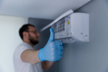 Mavi eldiven giyen bir teknisyen, bir havalandırma ünitesi kurduktan sonra konut alanında iyi yapılmış bir işten memnun olduğunu gösteren bir onay gösteriyor..