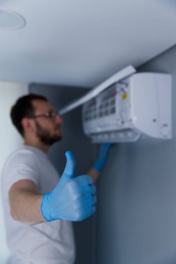 Mavi eldiven giyen yetenekli bir teknisyen, klima ünitesinin yanında duruyor ve şık bir iç mekanda başarılı bir kurulum olduğunu gösteren bir jest yapıyor..