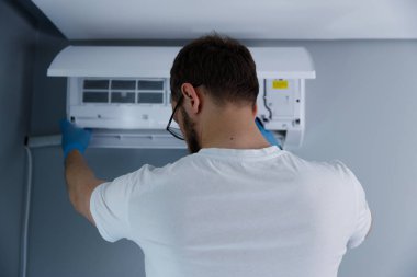 Beyaz gömlek ve mavi eldiven giyen bir şahıs, duvardaki havalandırma ünitesini düzelterek, profesyonellik ve dikkat göstererek, havalandırma bakımının detaylarına dikkat eder..