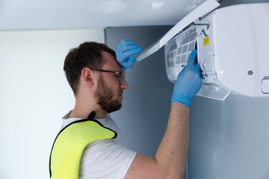 Mavi eldivenli odaklanmış bir teknisyen havalandırma ünitesi üzerinde çalışırken, HVAC sistemlerinde uzmanlık göstererek binalardaki etkili soğutma çözümleri için gerekli bakımı sağlıyor..