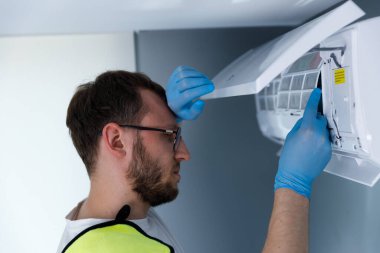 Mavi eldiven giyen odaklanmış bir teknisyen içeride bir havalandırma ünitesini inceliyor. Düzenli bakımın, bileşenleri dikkatle kontrol ederken, HVAC sistemleri için önemi açıktır..