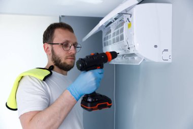 Yetenekli bir teknisyen, matkap kullanarak bir havalandırma ünitesini dikkatlice koruyor. Görevine odaklanmış durumda, düzgün yerleştirilmesini sağlıyor, koruyucu giysiler giyerken..