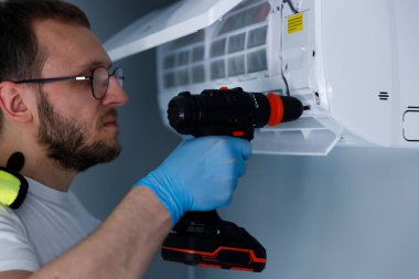 Yetenekli bir teknisyen bir klimayı tamir etmek için matkap kullanır. Eldivenler ve güvenlik teçhizatı ile donatılmıştır. Bu da HVAC bakımına profesyonel bir yaklaşım sağlar..