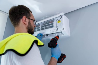 Yetenekli bir teknisyen bir havalandırma ünitesinde çalışıyor. Parçaları güvene almak için matkap kullanıyor. Bu bakım, evlerde veya ofislerde hava kalitesinin ve verimliliğinin artmasına yardımcı olur.