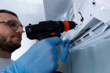 Yetenekli bir teknisyen, bir klima ünitesinin bakımını üstlenmek için elektrikli matkap kullanır. Ev aletleri servisinde hassasiyet, bakım ve uzmanlığın önemini gözler önüne serer..