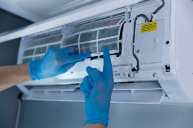 Mavi eldiven giyen yetenekli bir teknisyen bir havalandırma ünitesinin filtrelerini kontrol ediyor. Düzenli bakımın ideal performans ve temiz hava dolaşımı için önemini vurguluyor..