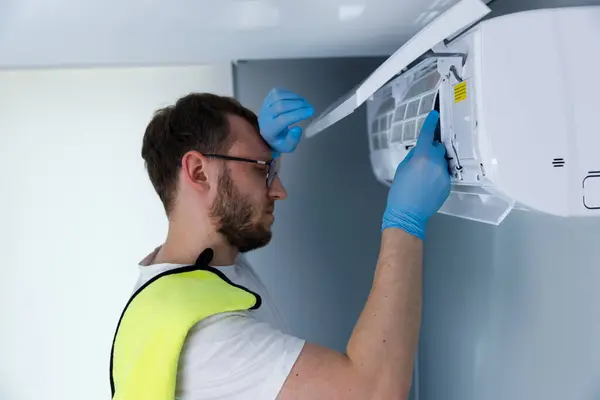Mavi eldivenli odaklanmış bir teknisyen havalandırma ünitesi üzerinde çalışırken, HVAC sistemlerinde uzmanlık göstererek binalardaki etkili soğutma çözümleri için gerekli bakımı sağlıyor..