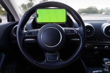 Bu resim modern bir arabanın içini gösteriyor, şık bir tasarımı olan direksiyon simidini vurguluyor ve yukarıdaki parlak yeşil ekranı kolayca erişebilmek için üzerine monte ediyor..