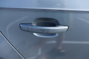 Bu resim, otomotiv mühendisliğinde kullanılan tasarım unsurlarını ve işçiliğini vurgulayan, gösterişli gri bir aracın arka planına karşı yapılmış bir araba kapı kolunun yakın plan perspektifini gösteriyor..