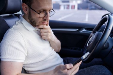 Düşünceli genç bir adam arabada oturmuş, öne eğiliyor ve akıllı telefonunu kullanıyor, her gün teknolojiyle bir anlık bir düşünce ya da çatışma sergiliyor..