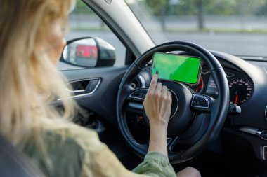 Bu resim, araba kullanırken akıllı telefonuna odaklanmış, arabalardaki modern dikkat dağıtıcı şeyleri ve dijital çağda yol güvenliğinin önemini vurgulayan bir kadını tasvir ediyor..