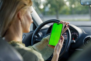 Arabadaki bir kadın, tek eliyle direksiyonu kavrarken elinde parlak yeşil bir ekran olan akıllı bir telefonla bağlantı ve güvenli sürüş pratikleri arasındaki dengeyi vurguluyor..