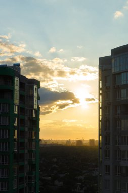Gün batımının nefes kesici görüntüsü gökyüzünü iki uzun bina arasındaki sıcak renklerle aydınlatıyor, şehir manzarasının güzelliğini ve sakin akşam atmosferini yakalıyor..