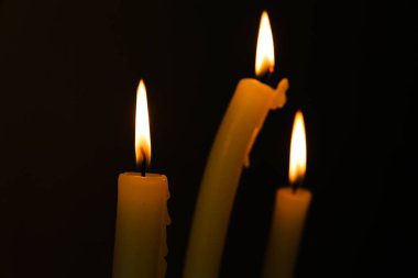 Bu görüntü, karanlık bir arkaplana yerleştirilmiş üç mum içeriyor. Ilık ışıltılarıyla çevreyi aydınlatıyor. Huzur ve tefekkür havasını artırıyor..