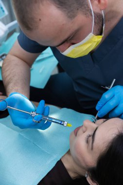Modern dişçilikte titiz teknikler sergileyen, klinik bir ortamda bir hastanın üzerinde şırınga kullanan bir diş hekimi tedavisi..
