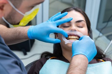 Bu diş sağlığı kliniği görüntüsünde, bir diş hekimi hastanın dişlerini dikkatlice inceler, ağız sağlığı ve hijyene önem verir ve prosedür sırasında hasta rahatlığı ve güvenliğine odaklanır..