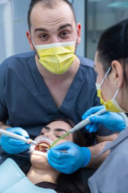 Yetenekli bir diş hekimi, klinik bir ortamda etkili tedavi ve bakım için modern diş aletlerini kullanırken, hasta rahatlığı ve temizliği sağlayan bir prosedür uyguluyor..