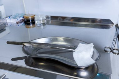 Bu resim, klinik bir ortamda cerrahi prosedürlere hazırlanan cımbız ve gazlı bez gibi temel tıbbi gereçleri içeren bir cerrahi tepsi sergiliyor..