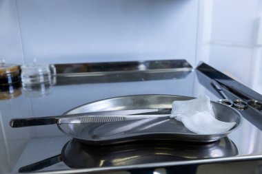 Görüntü, temiz paslanmaz çelik cerrahi tepsiyi cımbız ve gazlı bez de dahil olmak üzere hassas aletlerle gösteriyor. Hijyen üzerine odaklanmış titiz bir tıbbi çalışma alanını yansıtıyor..