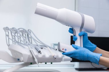 Bu görüntüde, mavi eldivenli bir diş hekimi diş prosedürleri sırasında hasta deneyimini ve güvenliğini geliştirmek için tasarlanmış modern teknolojiyi gösteren yüksek teknolojili bir diş aleti tutuyor..