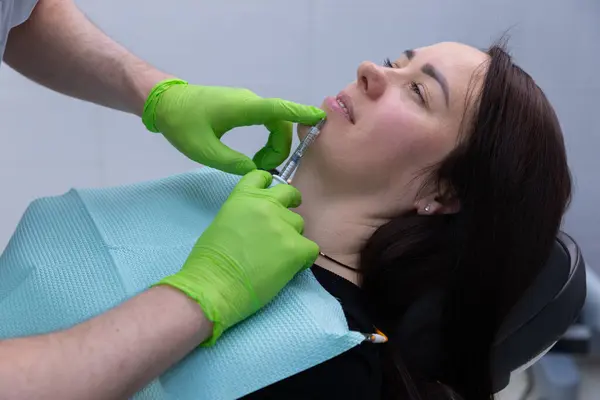 Modern bir klinikte, yetenekli bir profesyonel hastanın yüz hatlarını hassasiyet ve özenle geliştirmek amacıyla çenesine bir kozmetik dolgu yapar..