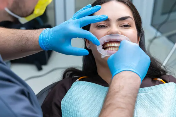 Bu görüntüde, hastaya rutin bir muayene ya da tedavi uygulayan bir diş hekimi, dişçi aletleri ve oral sağlığı vurgulayan profesyonel bir klinik seti yer alıyor..