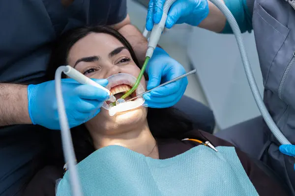 Bu görüntüde, bir hasta ileri diş aletleri kullanarak profesyonellerle diş tedavisi görüyor. Hasta rahatlamış görünüyor ve bu süreçte aktif olarak meşgul..