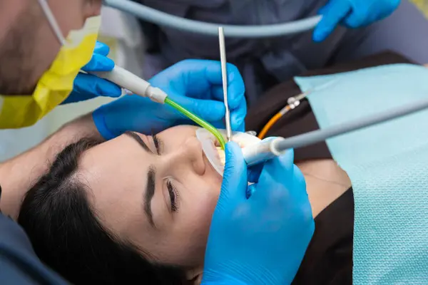 Görüntü, diş hekimliğinin geliştirilmesi ve konforun geliştirilmesi için modern teknikler kullanan ve gevşemiş görünen bir hasta üzerinde gelişmiş diş aletleri kullanan bir dişçiyi gösteriyor..