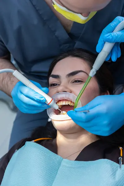 Bu görüntü, dişçi olarak yalan söyleyen bir hastanın dişçi aletlerini kullanarak dişçilik yaptığı ve her ikisinin de uygun koruyucu giysiler giydiği bir diş prosedürünü gösteriyor..