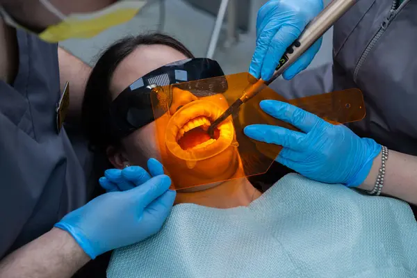 Diş tedavisi gören, koruyucu gözlüklerle donatılmış ve profesyonellerle çevrili bir hasta, çağdaş diş hekimlerinde bakım ve teknolojinin karışımını sergiliyor.