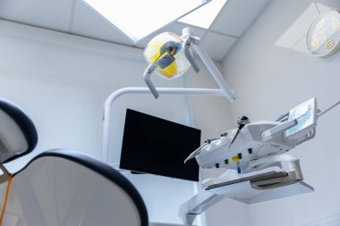 Görüntü, çeşitli diş aletleri, rahat bir sandalye ve parlak, doğal ışıklandırmanın hastalar için hoş bir ortam oluşturduğu modern bir diş muayenehanesini gösteriyor..