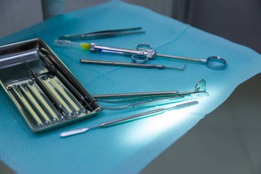 Profesyonel bir klinik ortamında dişçi muayenesi ve tedavileri için kullanılan temel ekipmanların altını çizerek, mavi bir yüzey üzerinde titizlikle düzenlenmiş bir diş aletleri dizisi.