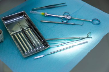 Görüntü, steril, açık mavi bir bez üzerinde titizlikle düzenlenmiş aynalar ve pullar da dahil olmak üzere bir dizi temel diş aletini gösteriyor..