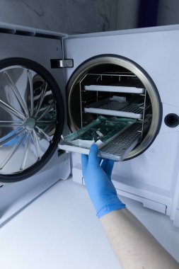 Bu görüntü, mavi eldivenli bir kişinin vakum odasından içinde cam eşyalar bulunan bir tepsiyi nazikçe çıkardığı bir laboratuvar ortamını yakalar..