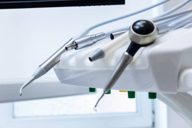 Bu resim, diş sandalyesine bağlı gelişmiş diş aletlerinin yakın çekimini gösteriyor, bugün oral sağlık hizmetlerinde kullanılan gelişmiş araçları vurguluyor..