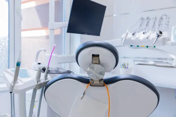 Görüntü, rahat bir diş sandalyesine, gelişmiş diş ekipmanlarına ve geniş ekrana sahip, hastalar için davetkar ve profesyonel bir atmosfer yaratan şık ve modern bir diş muayenehanesini gösteriyor..